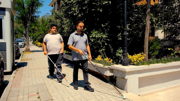 Engelsiz Erişim Derneği'nin iki üyesini beyaz bastonları ile sokakta yürürken gösteren bir fotoğraf